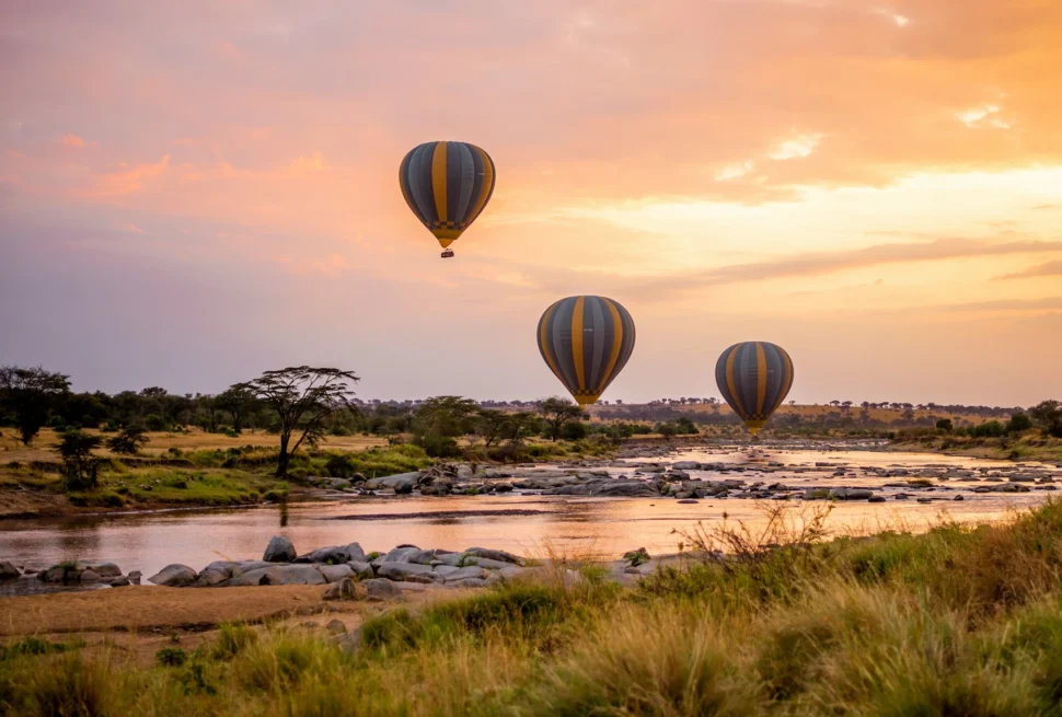 Wide-angle view of hot air safari baloons on open East African savannah grassland.